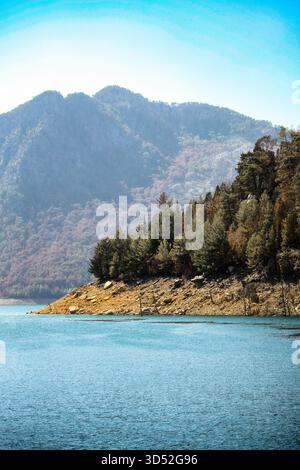 Vue verticale d'une péninsule rocheuse avec des pins s'étendant dans le réservoir turquoise sous un fond de montagne brumeux dans Green Canyon Banque D'Images