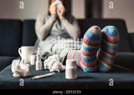 Grippe ou grippe. Malade et malade en hiver froid. Femme avec des chaussettes. Spray nasal pour le médicament contre les allergies ou la fièvre. Personne éternuant sur une serviette en papier. Banque D'Images
