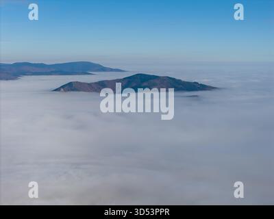 Vue aérienne des îles montagneuses traversant une mer de brouillard éthérée, éclairée par la douce lueur du soleil, Orschwiller, Grand est, France. Banque D'Images