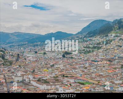 Vue aérienne des toits en terre cuite descendant la vallée en cascade vers le centre-ville, ombragé par les montagnes des Andes, Quito, Équateur. Banque D'Images
