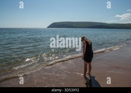 Vue arrière d'une femme mature dans une robe d'été pagayant dans l'eau peu profonde sur une plage en été, Colombie-Britannique, Canada Banque D'Images