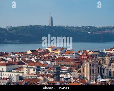Vue sur les toits rouges en cascade à travers le paysage urbain, menant le regard vers le Tage et la statue lointaine de Cristo Rei, Lisbonne, Lisbonne, Portugal. Banque D'Images