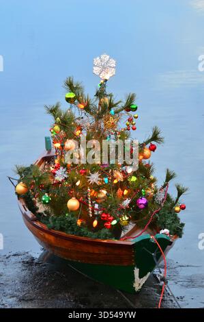 Une petite barque est décorée d'un joli arbre de Noël et amarrée sur le rivage pendant la saison des fêtes Banque D'Images