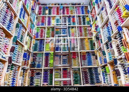 Fès, Maroc – exposition vibrante de rouleaux de tissus colorés soigneusement empilés dans un magasin de textile marocain traditionnel. Les étagères organisées et l'échelle en bois Banque D'Images