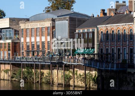 Les bâtiments bordent une rivière avec une passerelle piétonne sur pilotis bondés de dîners à York, Royaume-Uni. Banque D'Images