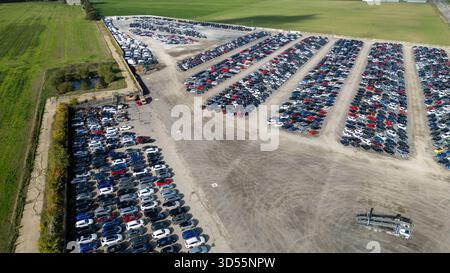 Une vue aérienne capture un grand terrain de stockage extérieur rempli de rangées de véhicules de différentes couleurs, bordé par des champs verts et un petit étang à Co Banque D'Images