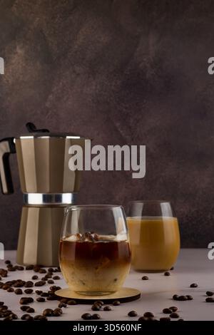 Une cafetière se trouve à côté de deux verres remplis de café infusé froid et de lait. Autour d'eux sont dispersés grains de café sur une surface sombre, créant un Banque D'Images