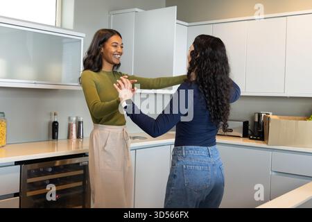 Danser diverses amies féminines se tenant la main dans la cuisine moderne, avec des bocaux en verre et une boîte d'épicerie Banque D'Images