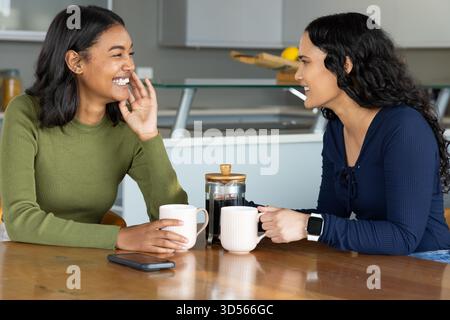 Souriant diverses amies féminines sirotant du café à la table de la cuisine à la maison, avec presse française et citrons Banque D'Images
