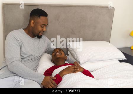 Père afro-américain réconfortant son fils au lit, partageant un moment joyeux à la maison Banque D'Images