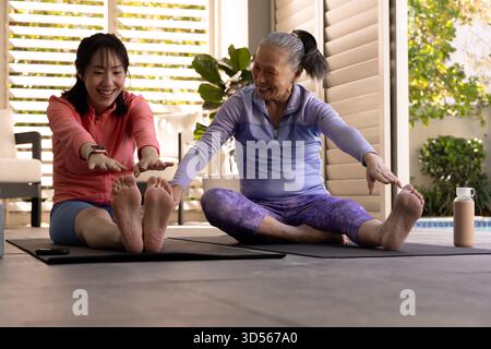 Mère aînée asiatique et fille faisant du yoga ensemble sur des tapis, souriant et s'étirant Banque D'Images