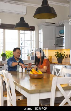 Couple asiatique mature appréciant le petit déjeuner ensemble à la maison dans une cuisine lumineuse Banque D'Images