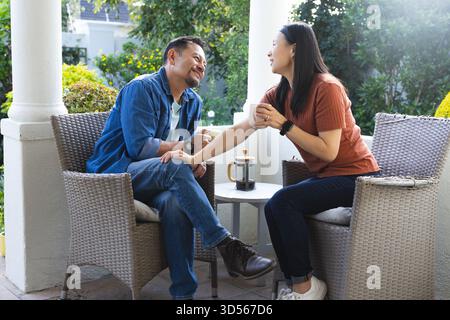 Couple asiatique mature appréciant le café et la conversation sur le patio, partageant le moment joyeux Banque D'Images