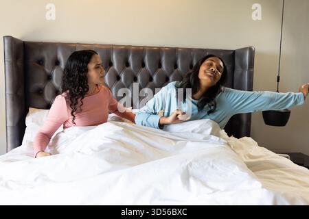 Assis divers partenaires féminins discutant et s'étirant sur le lit dans la chambre, avec tête de lit touffetée Banque D'Images