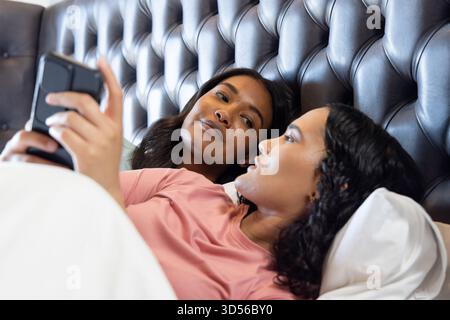 Relaxant divers partenaires féminins allongés sur le lit dans la chambre, avec smartphone et literie blanche Banque D'Images
