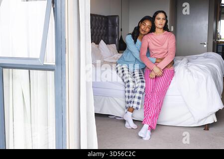 Embrasser divers partenaires féminins assis sur le bord du lit dans la chambre, avec des draps blancs Banque D'Images