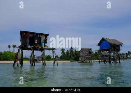 Semporna, Sabah, Malaisie - 7 novembre 2025 - les maisons traditionnelles sur pilotis de Bajau Laut se dressent au-dessus de l'eau près d'un rivage bordé de palmiers dans un vill isolé Banque D'Images