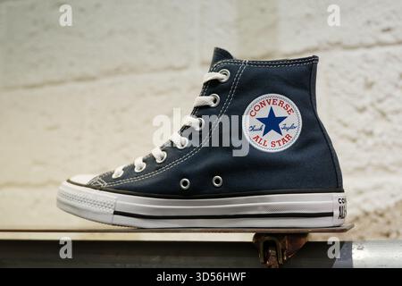 Une paire de sneakers montantes Converse All Star en toile bleu marine exposées sur une étagère en bois, arborant un logo rond Banque D'Images