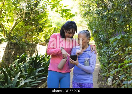 Pointant la mère et la fille chinoises asiatiques debout sur le chemin du parc, avec smartphone et bouteilles d'eau Banque D'Images