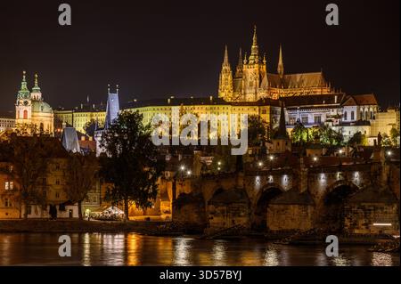 Vue du château de Prague illuminé la nuit prise sur la rivière Vltava avec le pont Charles au premier plan Banque D'Images