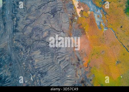Le drone abstrait a tracé une frontière nette entre deux paysages distincts : un sol gris fortement érodé ou industriel avec des textures complexes et des marais aux couleurs vives jaune, orange et vert Banque D'Images