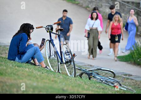Angers (nord-ouest de la France) : jeune cycliste assise sur une pelouse en pente à côté de son vélo, parlant à son amie sur un smartphone via un appel vidéo. G Banque D'Images