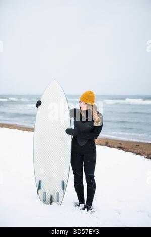 Femme solo avec planche de surf sur la plage enneigée en hiver Banque D'Images