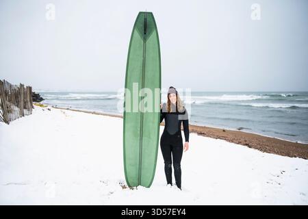Femme solo avec planche de surf sur la plage enneigée en hiver Banque D'Images