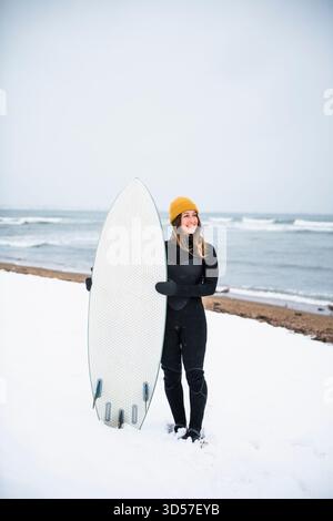 Femme solo avec planche de surf sur la plage enneigée en hiver Banque D'Images