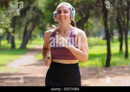 Jeune femme faisant du jogging à l'extérieur sur le chemin du parc portant des vêtements de sport et des écouteurs Banque D'Images