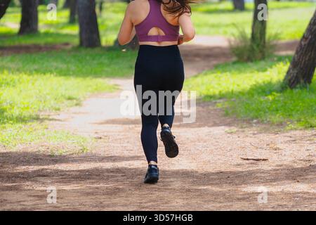 Vue arrière de la femme sportive courant à l'extérieur sur le chemin dans l'exercice de parc vert Banque D'Images