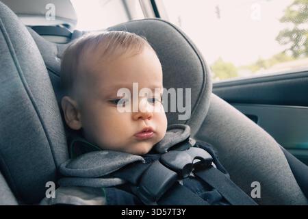 Portrait en gros plan d'un bébé garçon assis dans un siège d'enfant à l'arrière d'une voiture Banque D'Images