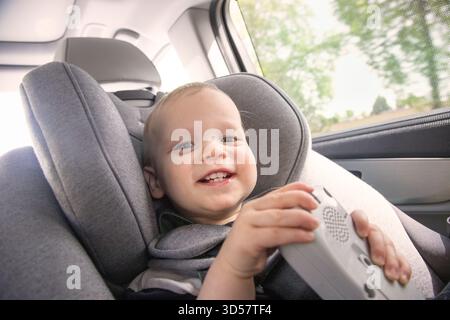 Bébé garçon souriant assis dans un siège d'enfant à l'arrière d'une voiture tenant un jouet Banque D'Images