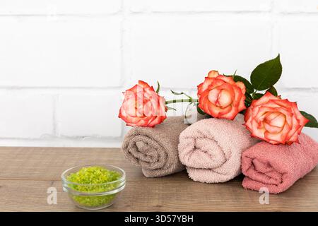Spa composition with soft terry towels, red rose flowers and a bowl of sea salt on the wooden floor. Banque D'Images