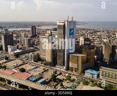 Vue aérienne de gratte-ciel imposants perçant la ligne d'horizon, juxtaposés au paysage urbain tentaculaire et à l'océan scintillant au loin, Lagos, Banque D'Images