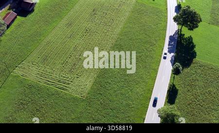 Voitures roulant sur une route rurale entre des champs verts avec des modèles de tonte récente, mettant en valeur les voyages de campagne et l'agriculture Banque D'Images