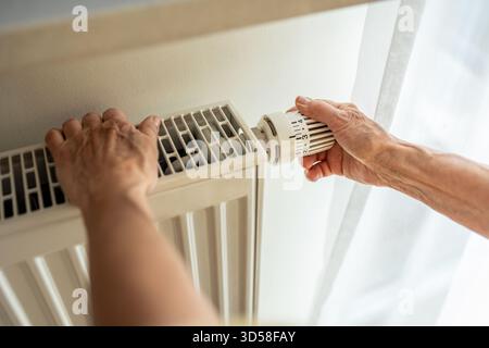 Femme âgée ajustant le chauffage sur un radiateur dans sa maison, gros plan Banque D'Images
