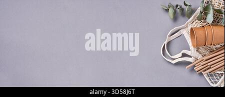 Boire des tubes bruns pailles en papier et fécule de maïs, sac de marché en maille et tasses à café en papier vides sur un fond gris à la mode. Zéro déchet et concept sans plastique. Vue de dessus. Banque D'Images