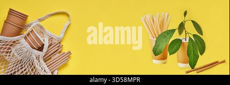 Boire des tubes bruns pailles en papier et fécule de maïs, sac de marché en maille et tasses à café en papier vides sur un fond gris et jaune tendance. Zéro déchet et concept sans plastique. Vue de dessus. Banque D'Images