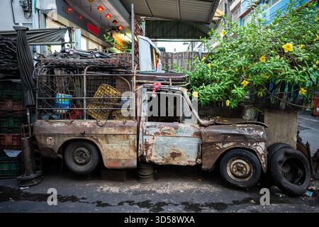 Vieille voiture rouillée détruite avec coffre plein de choses garé devant le bâtiment au coin de l'allée à Bangkok. Banque D'Images
