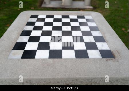 Échiquier en marbre extérieur sur la table en béton, les carrés altérés et les lignes épurées définies dans la pelouse calme du parc, espace de jeu vide suggérant la stratégie et PA Banque D'Images