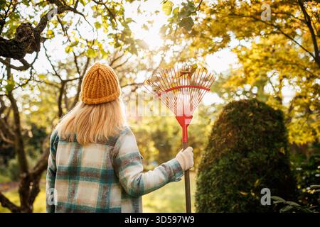 Jardinage à la saison d'automne. Femme jardinière avec râteau travaillant dans le jardin d'automne. Ratissage des feuilles tombées Banque D'Images