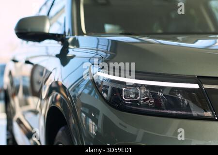 Gros plan montrant la face avant d'un VUS moderne garé à l'intérieur d'un concessionnaire automobile, reflétant les fenêtres et l'intérieur de la salle d'exposition, mettant l'accent sur les phares du véhicule et le design élégant de la carrosserie Banque D'Images