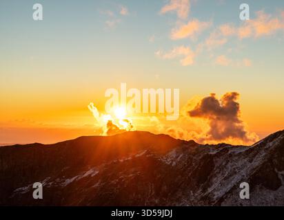 superbe coucher de soleil sur la chaîne de montagnes enneigées, avec des teintes orange et jaune vibrantes illuminant le ciel et les nuages, espace de copie de paysage Banque D'Images