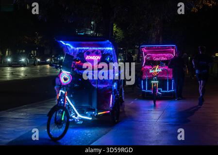 Pousse-pousse illuminés attendant les passagers à Westminster, Londres, Royaume-Uni, le soir. Pédicabs à louer, avec néons Banque D'Images