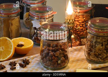 Biscuits et noix de Noël faits maison stockés dans des pots en verre avec une lampe à huile vintage et des oranges fraîches sur une table en bois rustique. Banque D'Images