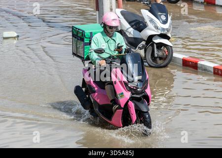 BANGKOK, THAÏLANDE, nov 09 2025, Un livreur sur un scooter rose traverse une rue inondée de la ville à l'aide d'un téléphone portable Banque D'Images