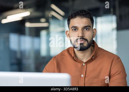 Homme d'affaires indien debout dans un bureau moderne, regardant la caméra avec l'expression sérieuse et confiante Smart-casual entrepreneur véhiculant professionnalisme, concentration et leadership Banque D'Images