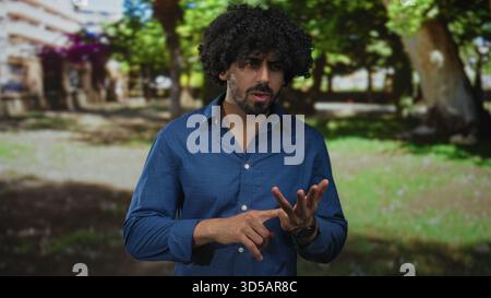 Homme dans une chemise bleue comptant sur ses doigts dans une scène de forêt parmi les arbres et l'herbe ; planification réfléchie. Banque D'Images