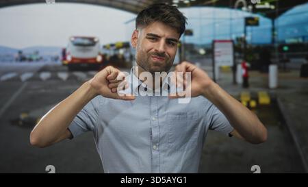 Homme tient la main dans les pouces vers le bas geste à l'extérieur terminal de l'aéroport occupé avec la navette derrière lui ; frustration. Banque D'Images